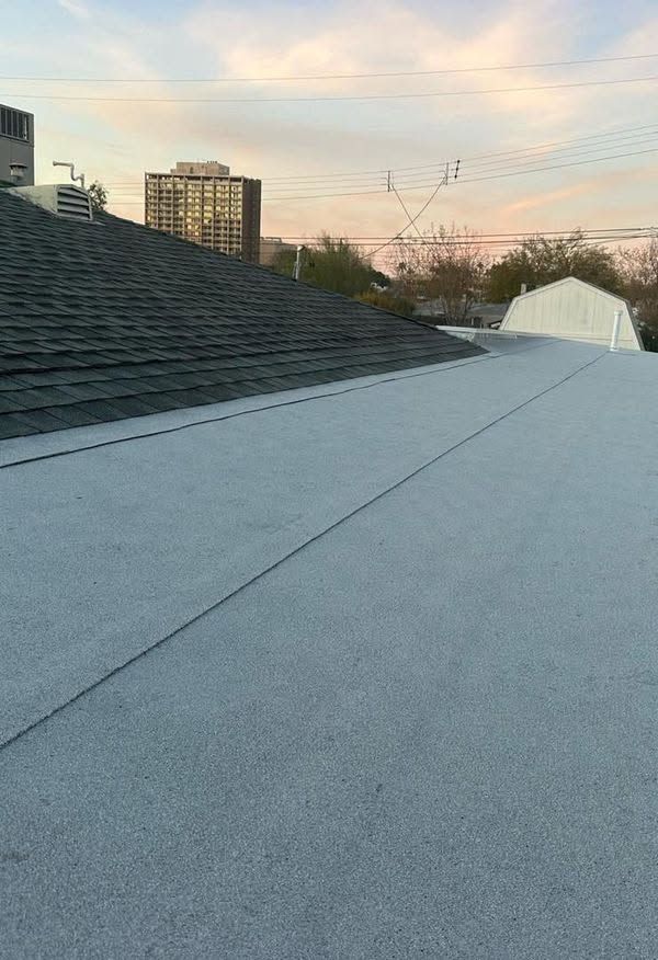 Rooftop with gray shingles at sunset, with city buildings and power lines in the background