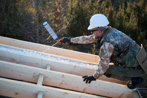 Worker in hard hat painting a slanted white structure outdoors with a roller