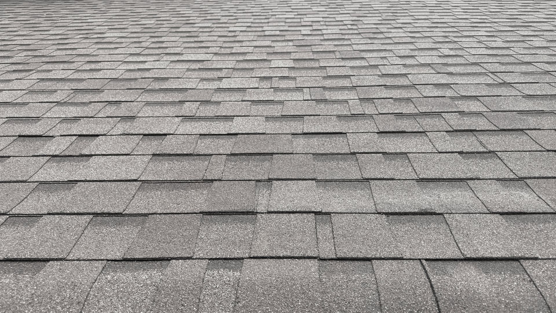 Gray asphalt roof shingles in a repeating pattern, viewed from above.