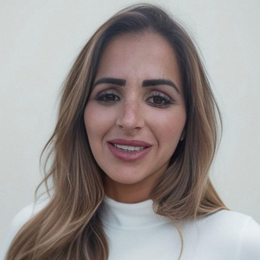 Woman with long, wavy blonde hair smiles at the camera, wearing a white turtleneck.