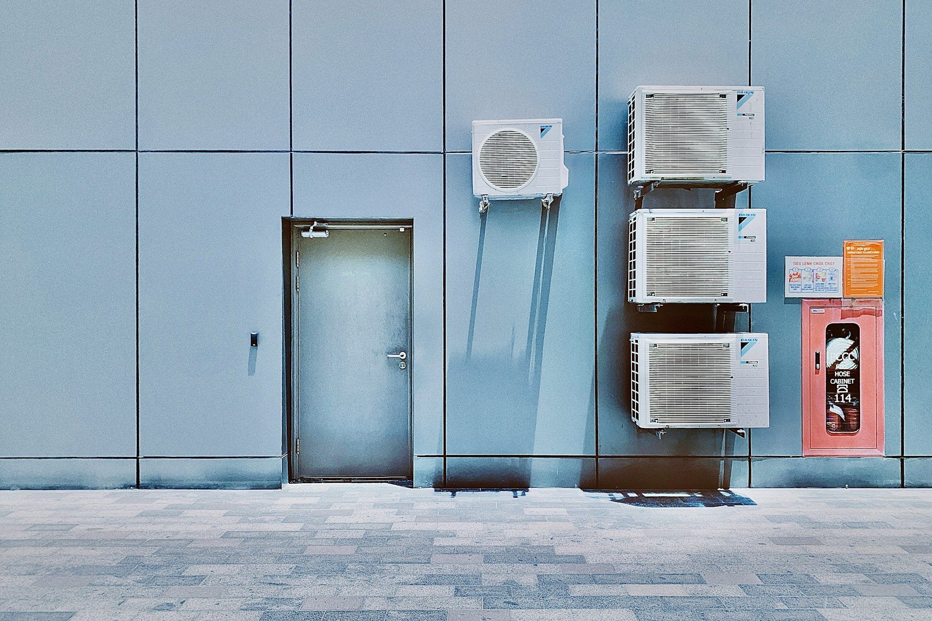 Blue industrial wall with a metal door, ventilation units, and a red fire extinguisher cabinet