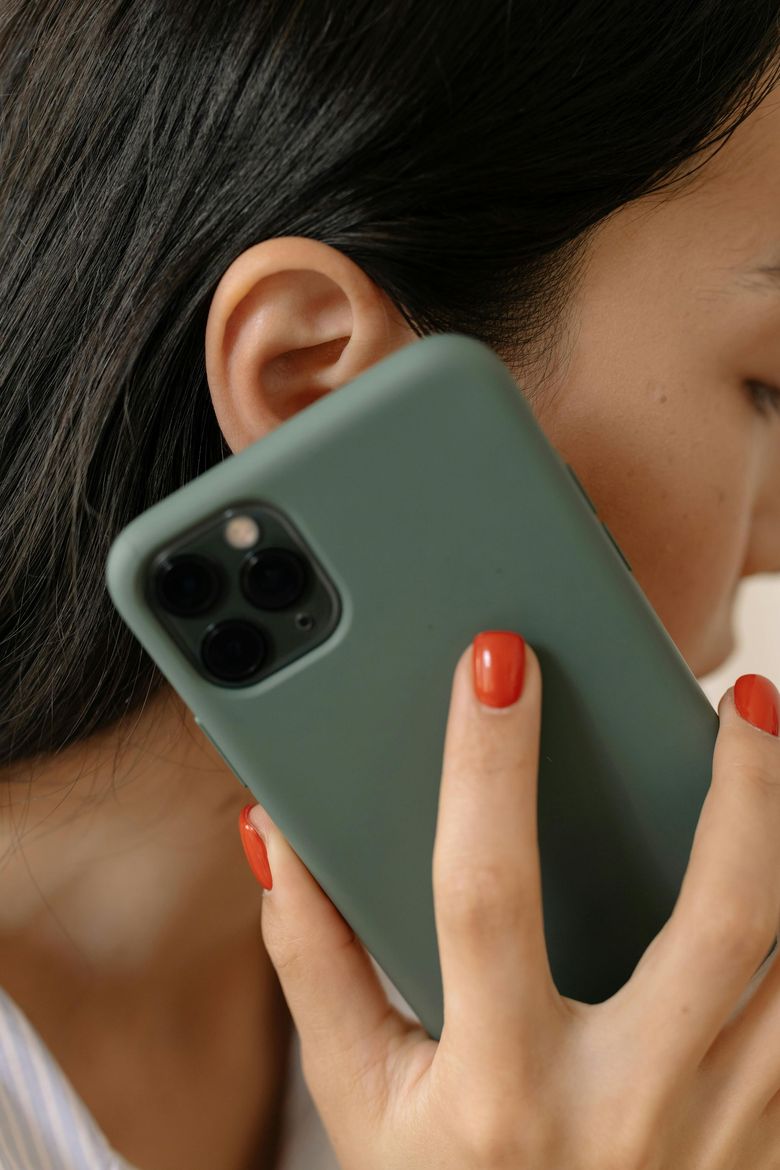 Woman holding a green smartphone to her ear, close-up with red-painted nails.