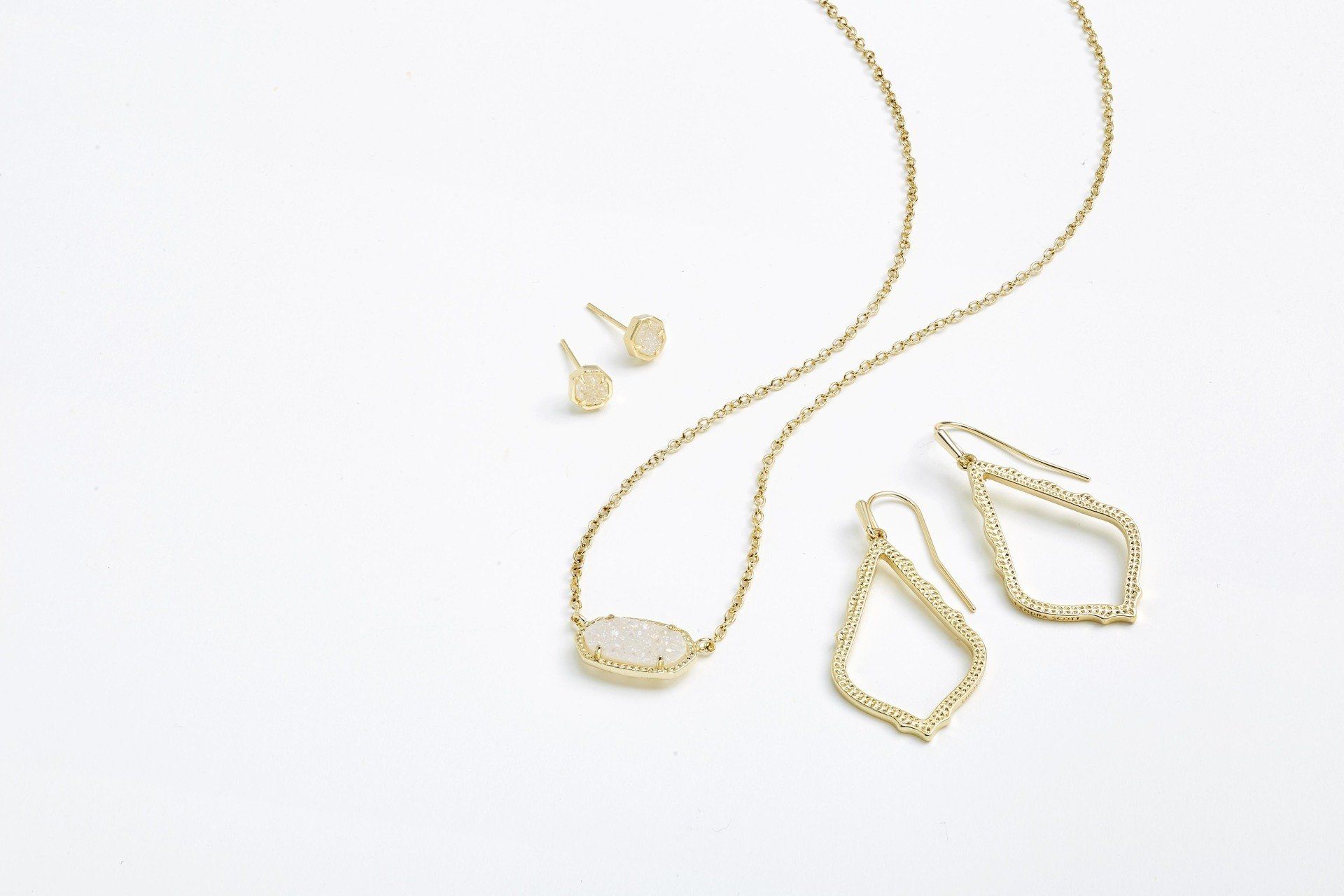 Gold jewelry set: necklace with gemstone, stud earrings, and drop earrings on white.