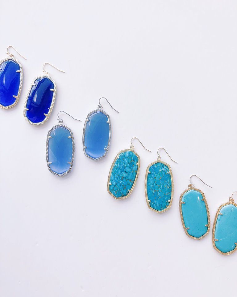 Six pairs of blue and turquoise rectangular drop earrings with gold-toned trim, against a white background.