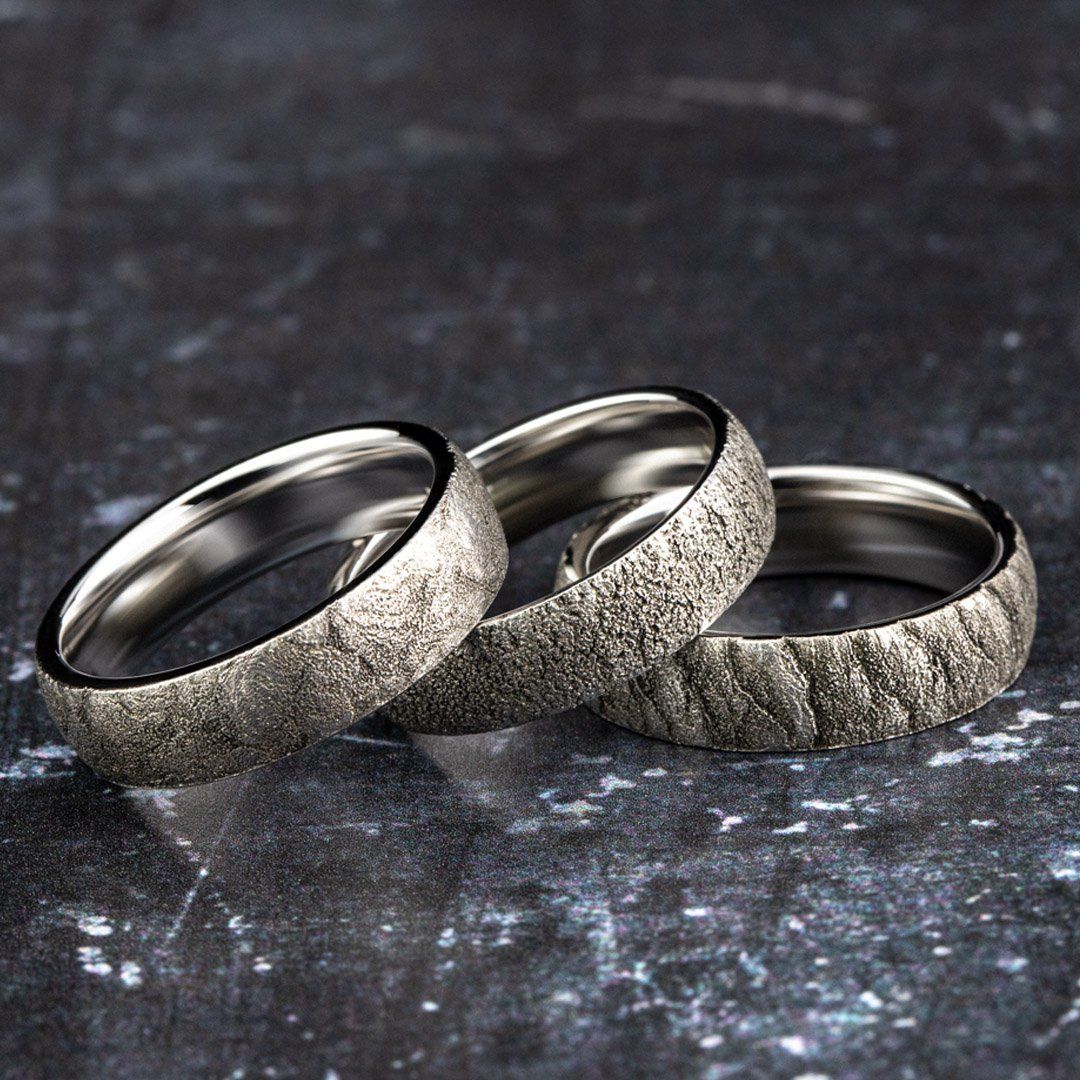 Three textured silver rings on a dark, mottled surface.