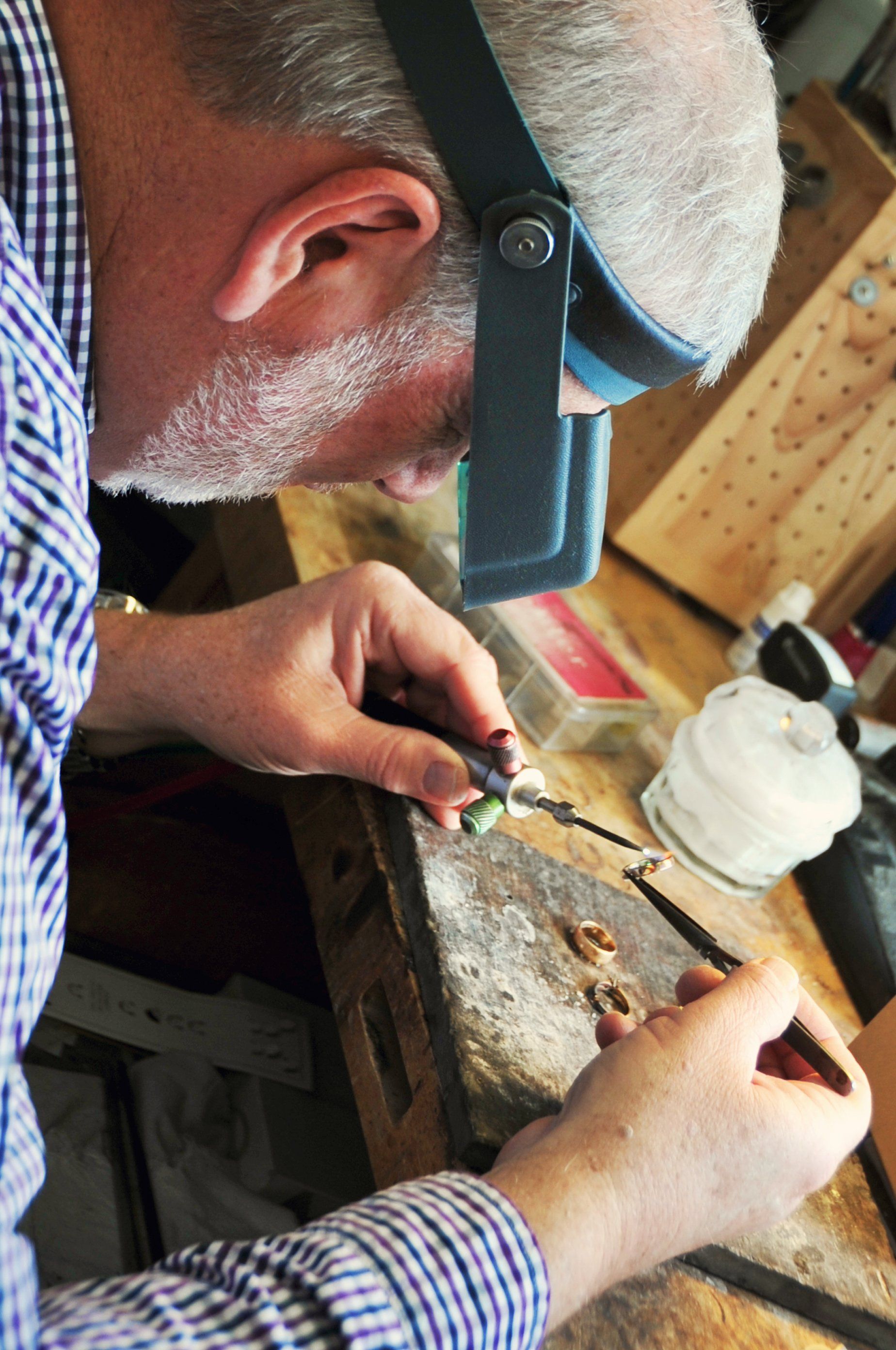 Jeweler working on small objects with tools, wearing a magnifying visor at a workbench.