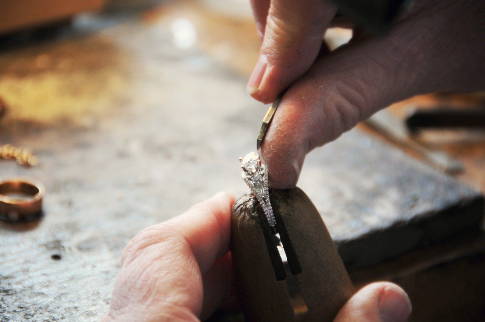 Jeweler uses tool to set a diamond in a ring, close-up shot. Focus on hands and ring on a work surface.