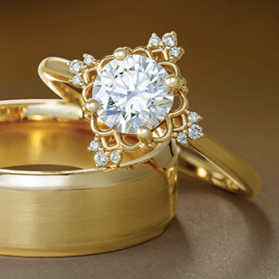 Gold engagement and wedding rings, diamond center stone, on a gold background.