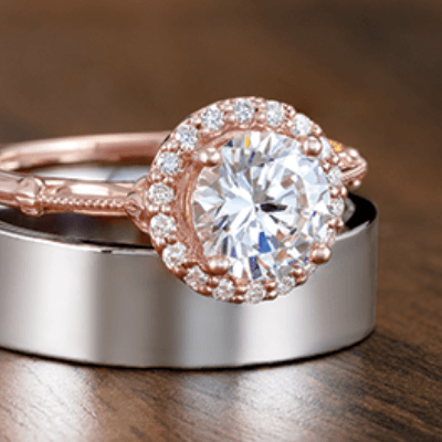 Rose gold halo engagement ring on top of a silver wedding band on a wooden surface.