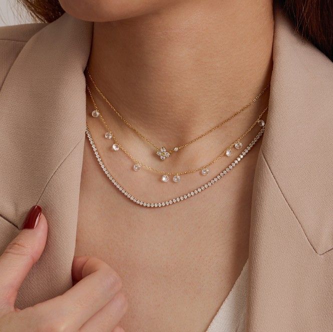 Woman wearing three layered gold necklaces with diamonds, against a beige blazer.
