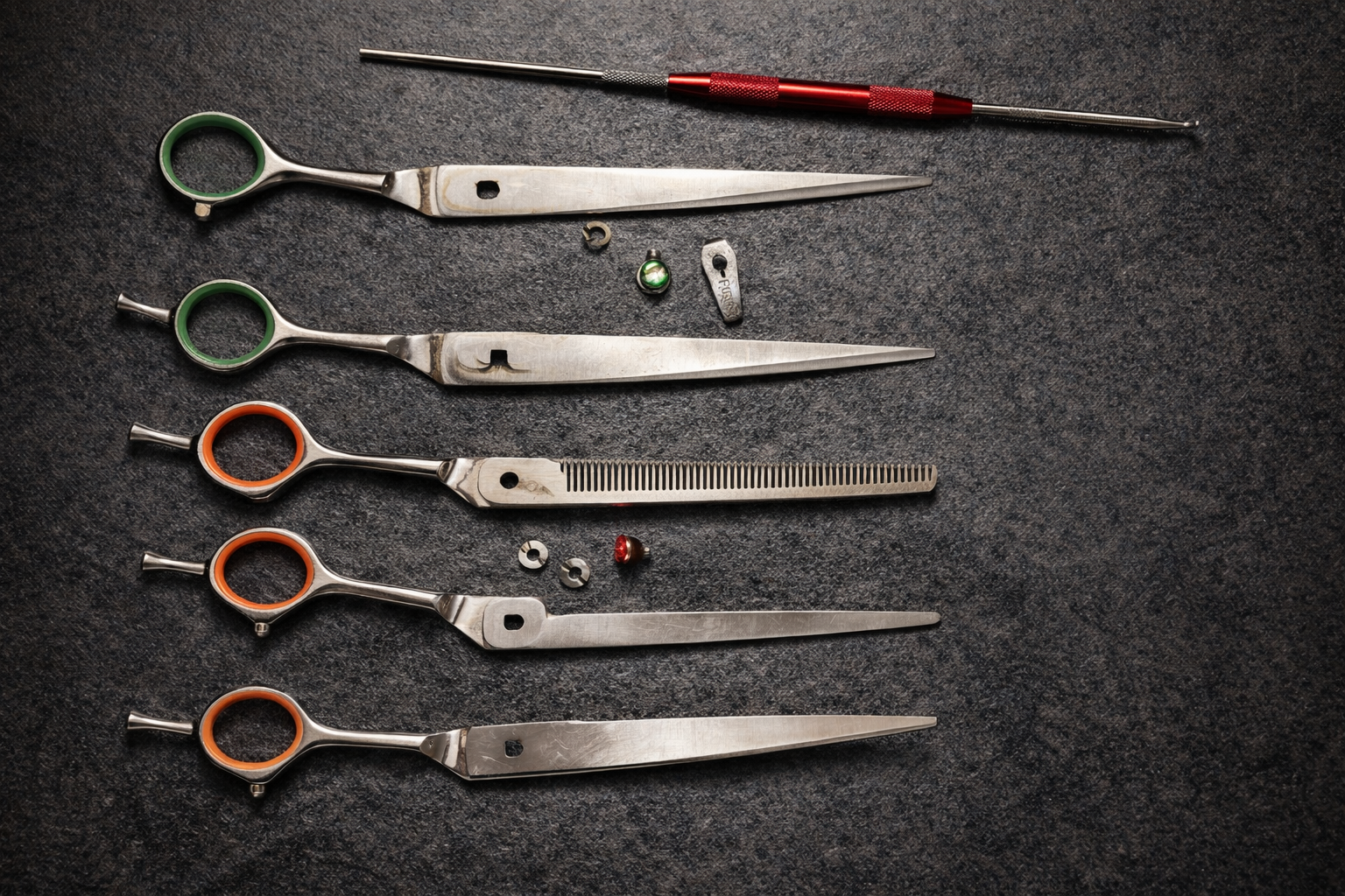 Grooming scissors and tools with colored finger holes, and a tool with a red handle lie on a dark surface.