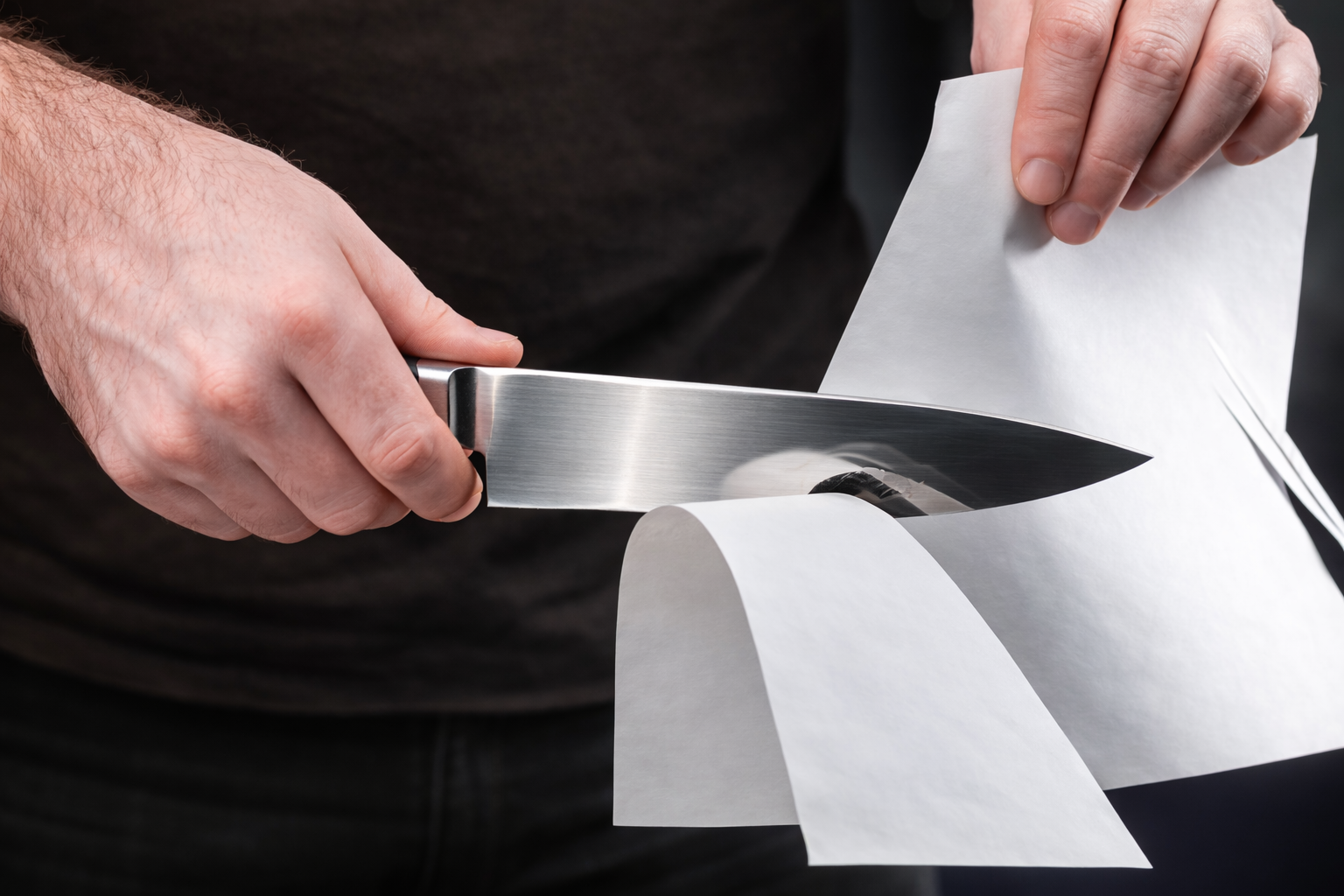 Person testing knife sharpness by slicing through paper.