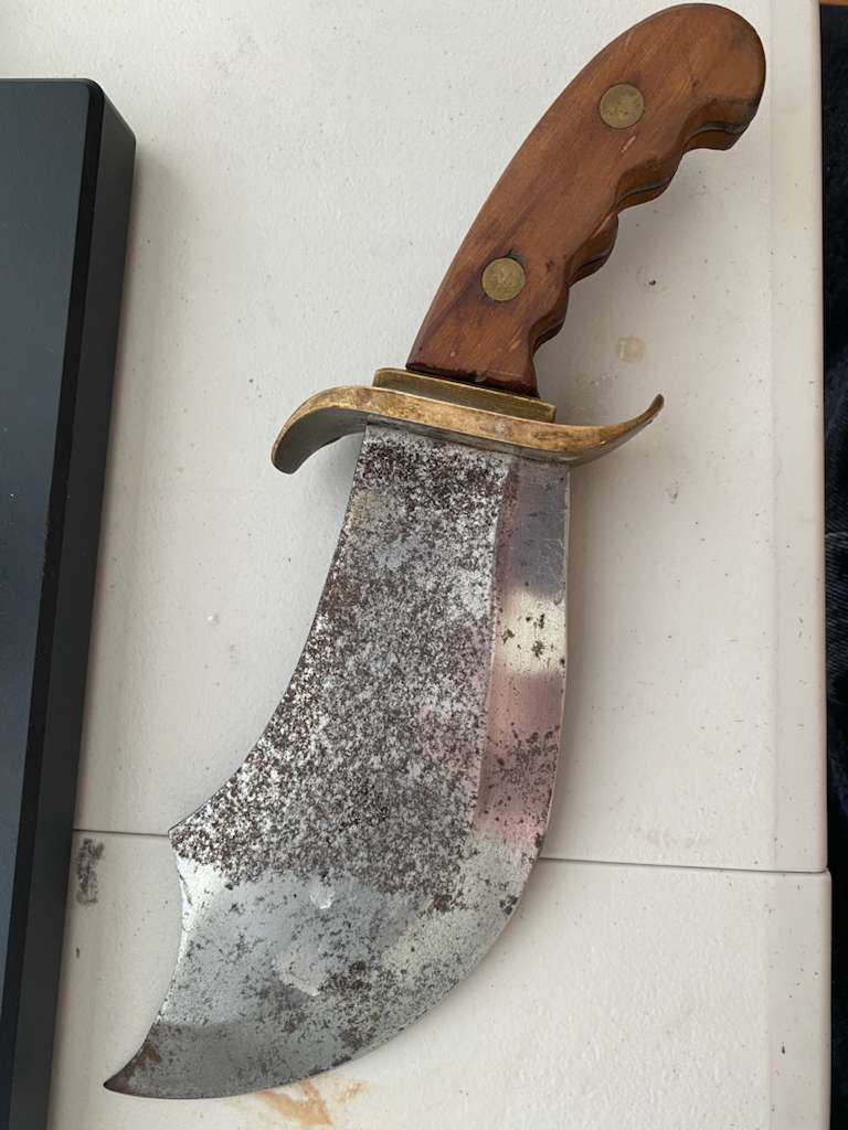 Large, curved knife with wooden handle, brass guard, and a tarnished blade.