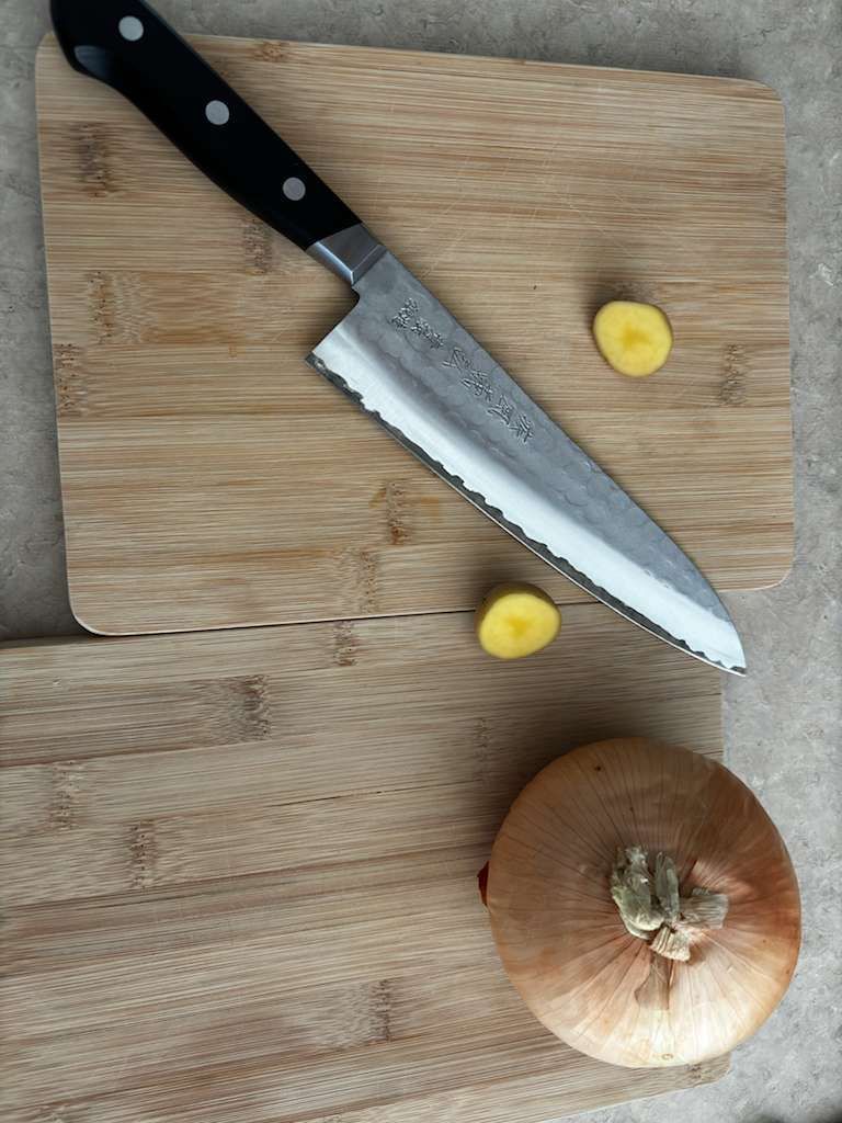 Knife on cutting board with onion and two ginger slices.