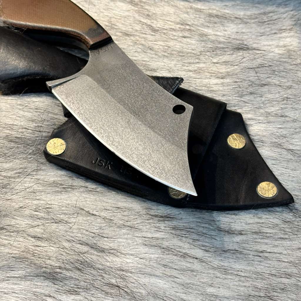 Butcher knife with a leather sheath on a textured surface.