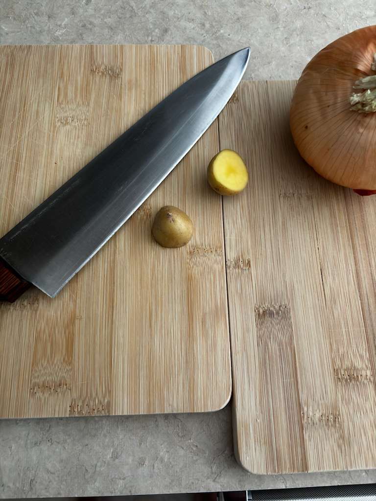 Knife, potato halves, and onion on bamboo cutting boards.