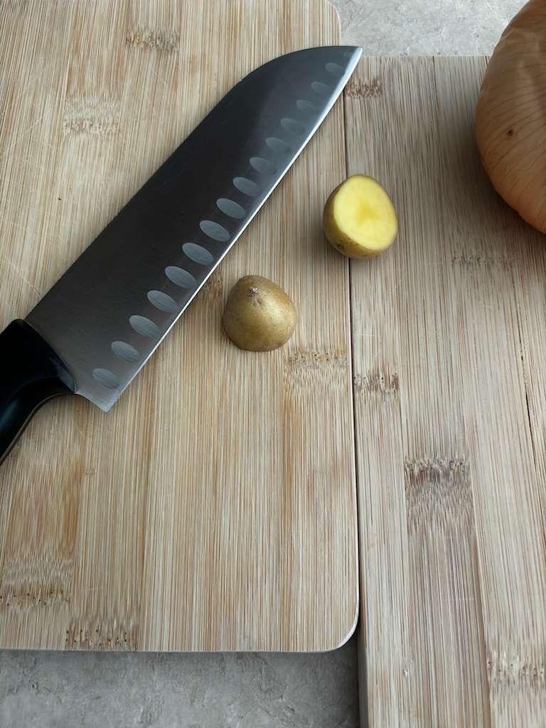 Knife on a wooden cutting board with two small potatoes, one cut open.
