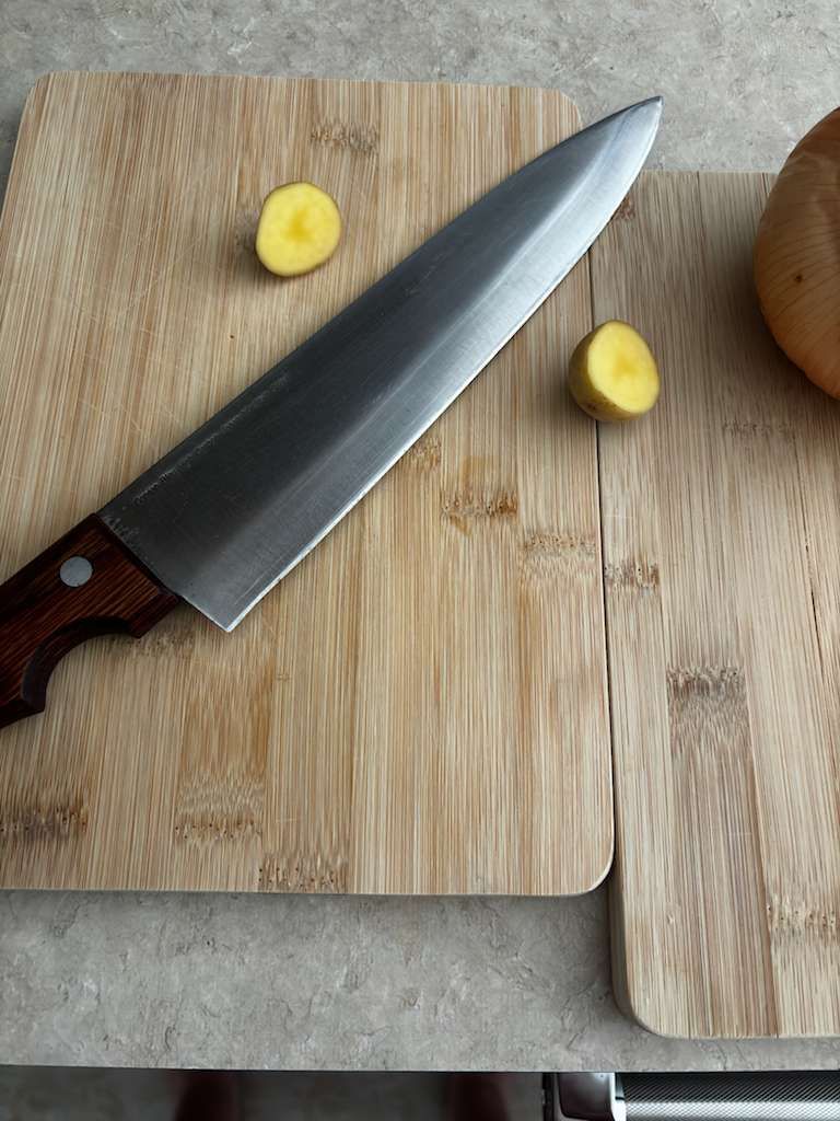 Chef's knife on a bamboo cutting board with two yellow vegetable slices and a squash.