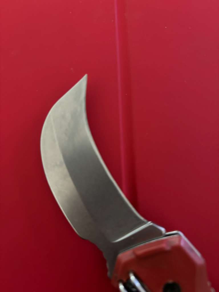 Curved metal blade knife against a red background.