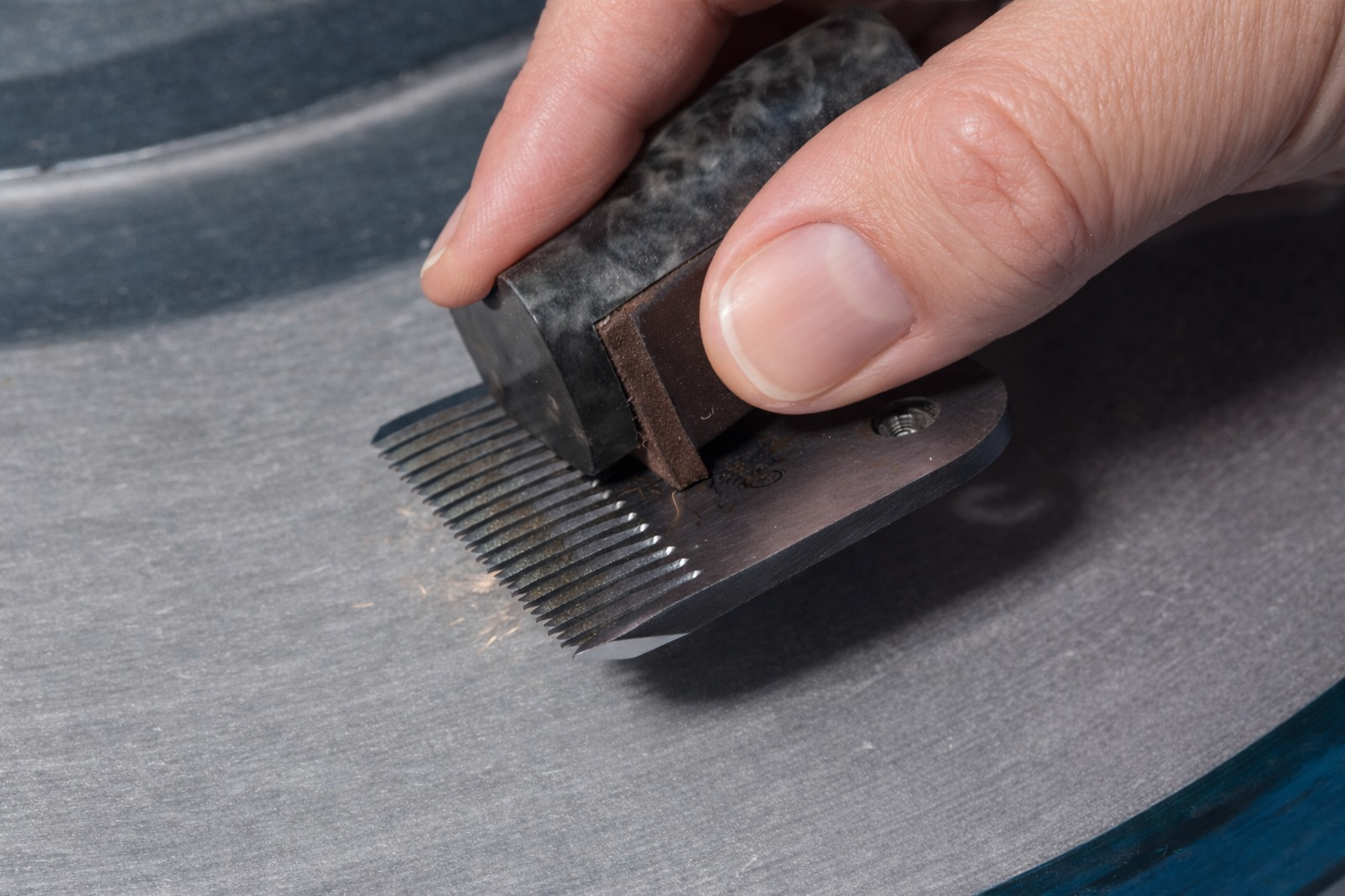 Hand sharpening a metal comb with a stone on a grinding wheel.