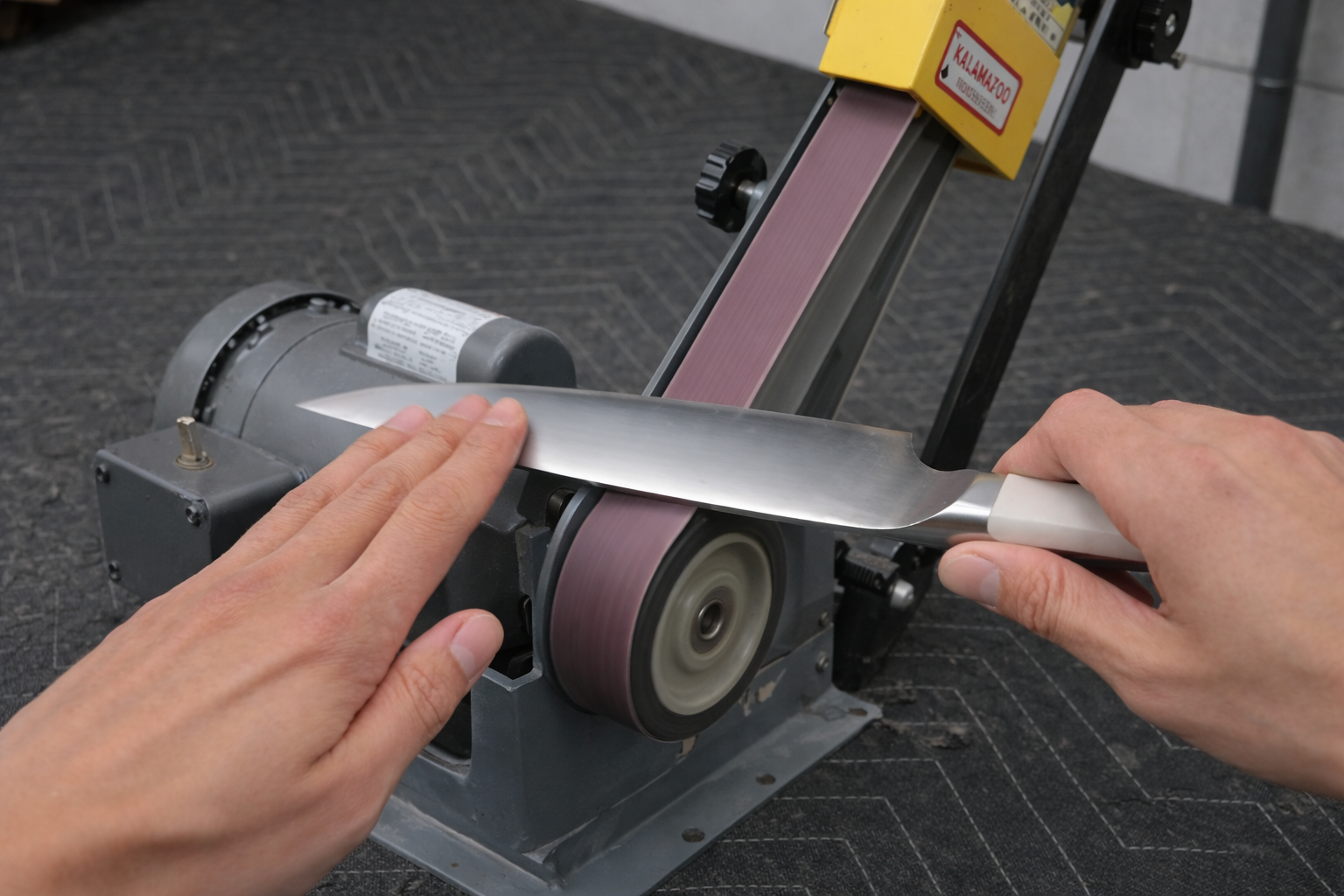 Person sharpening a knife blade on a grinding wheel, creating sparks, indoors.