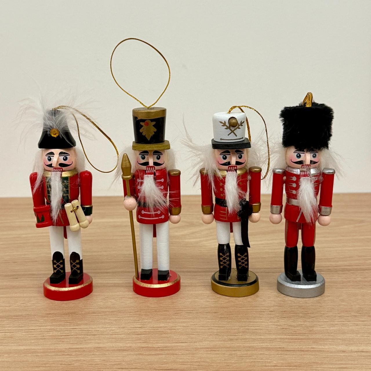 Cuatro adornos de cascanueces de madera en miniatura con abrigos rojos, sombreros negros y barbas blancas, sobre una superficie de madera.