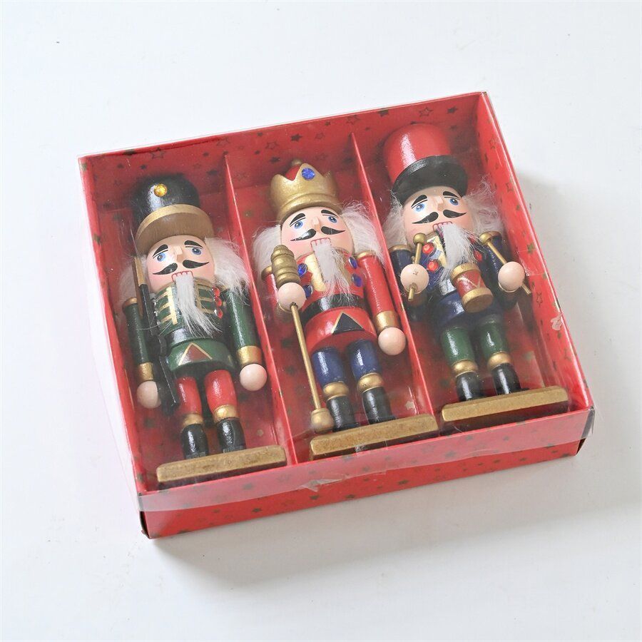 Tres cascanueces de madera de colores en una caja roja, sobre una superficie blanca.