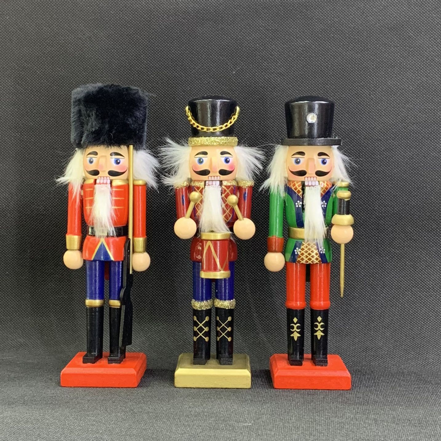 Tres cascanueces de juguete de color rojo, azul y verde con barbas blancas, colocados sobre pequeñas bases de madera.