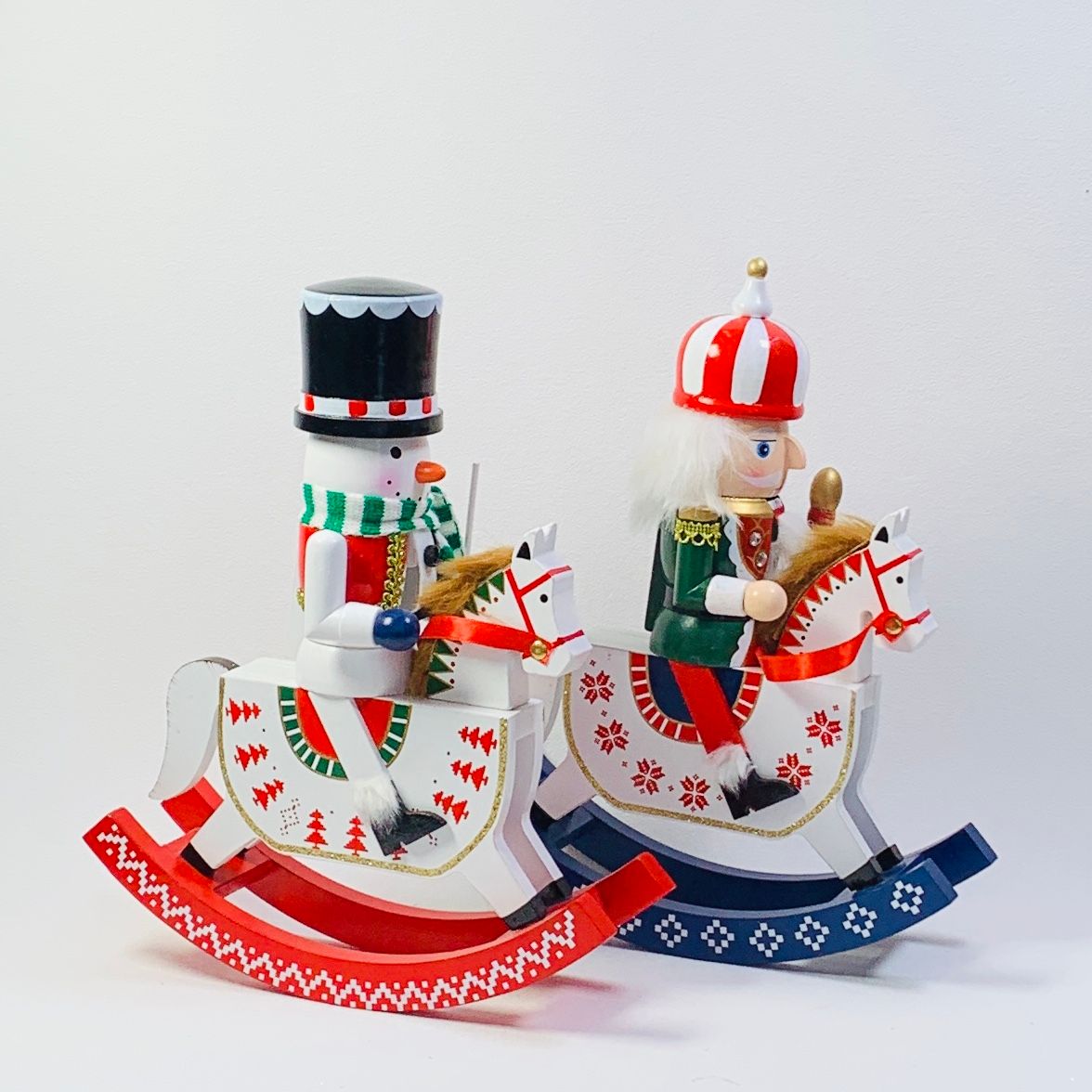 Dos figuras navideñas de cascanueces sobre caballos balancín, un muñeco de nieve y un soldado, festivos.