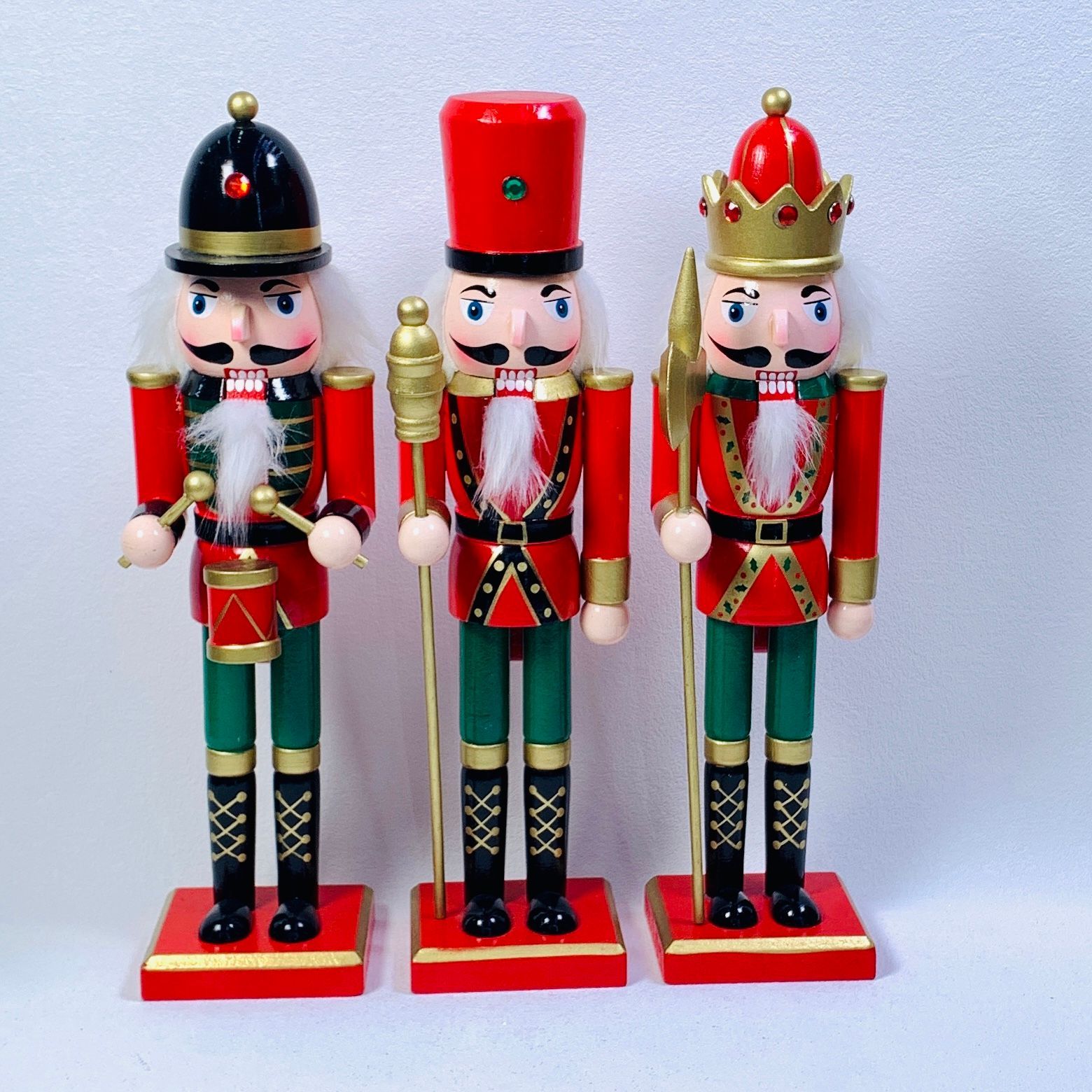 Tres figuras de cascanueces de madera de color rojo, verde y negro sobre bases rojas, sosteniendo herramientas y usando sombreros.