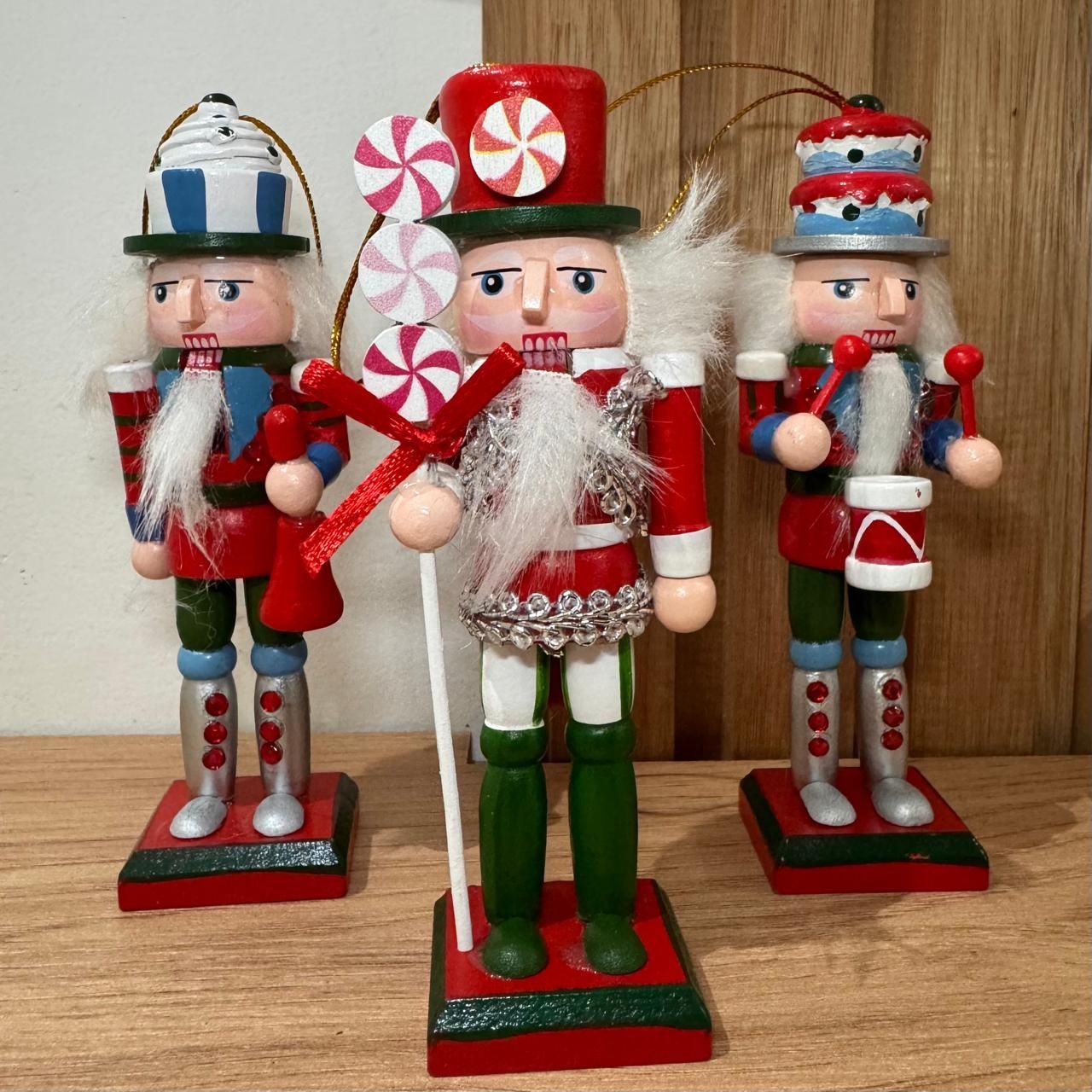 Tres figuras decorativas de cascanueces con detalles pintados en rojo, blanco, azul y verde, sosteniendo dulces, colocadas sobre una superficie de madera.
