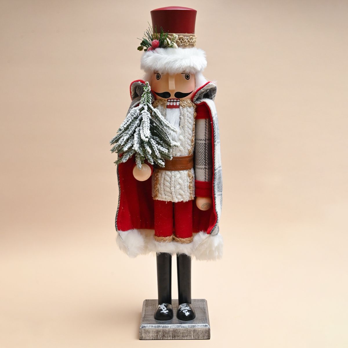 Figura de cascanueces navideño con capa roja y blanca, sosteniendo un árbol.