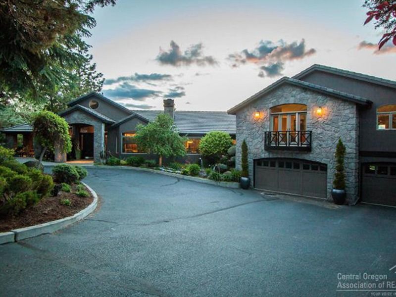 Luxury stone house exterior at dusk with curved driveway, lit windows, and landscaped greenery