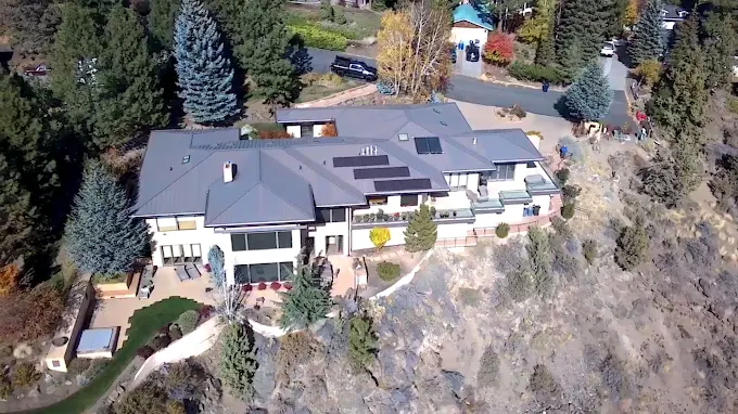 Aerial view of a large modern house with a gray roof on a wooded hillside.