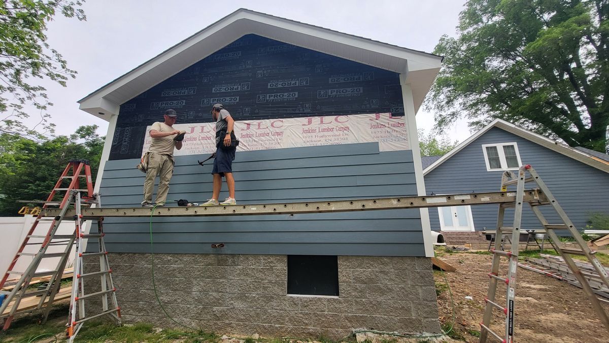 Two workers installing blue siding on a house. One is on a scaffold, the other on a ladder.