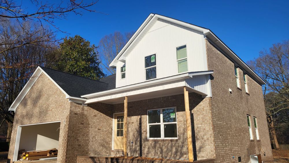 New two-story house under construction with brick exterior and white siding. Sunny, blue sky.