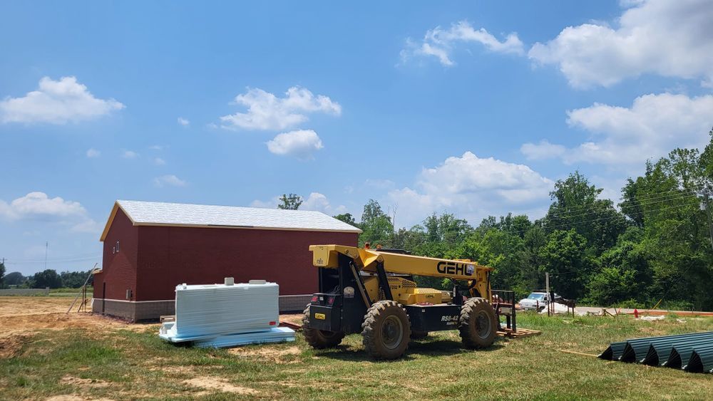 Red barn and yellow construction forklift on a sunny day with blue sky and some clouds.