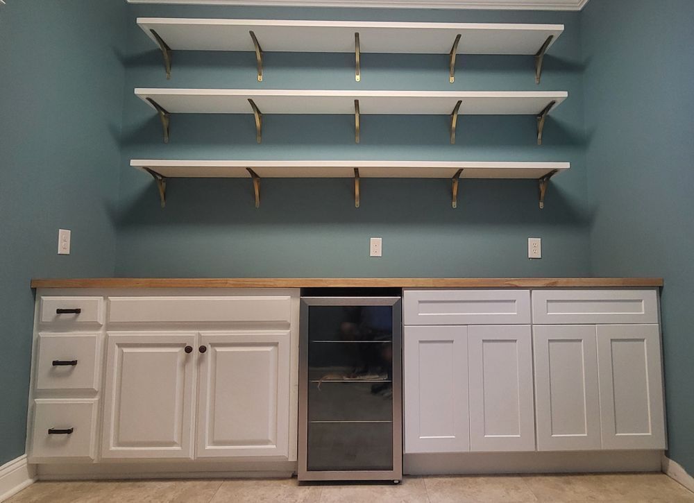 White shelving and cabinets with a beverage cooler on a blue wall.