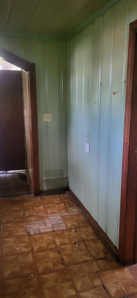 Entryway with light green paneling, wood trim, and damaged tile flooring.