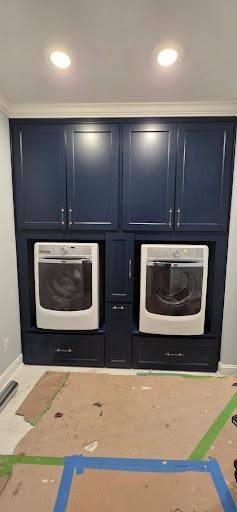 Built-in laundry appliances with blue cabinetry in a room with unfinished flooring.
