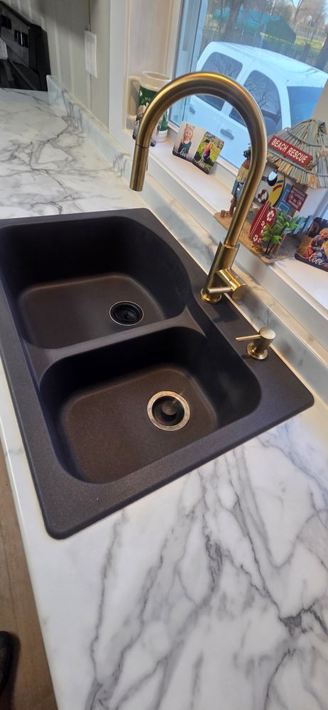 Black double sink with a gold faucet on a marble countertop.