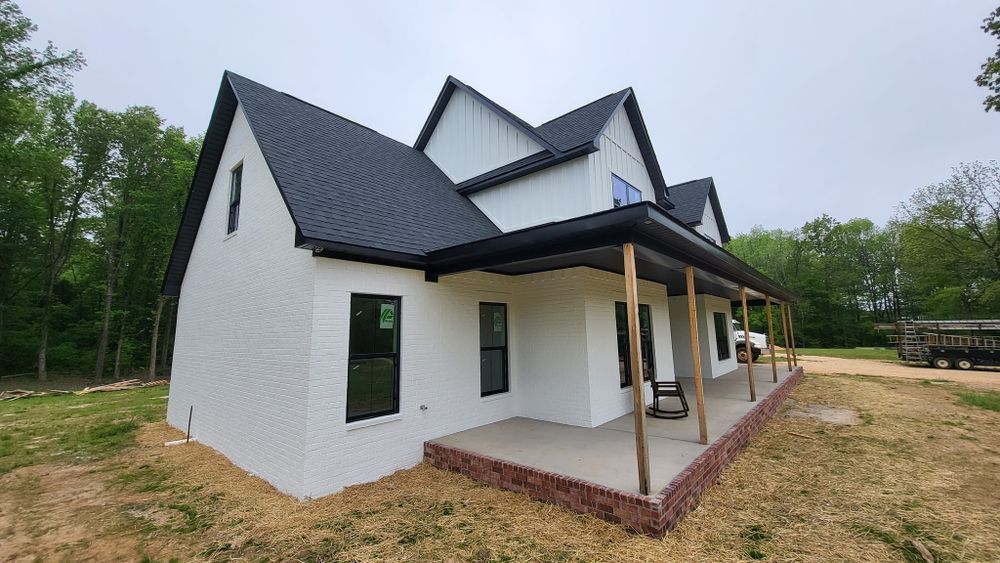 White farmhouse with black roof, trim, and windows, porch with wooden posts, under cloudy sky.