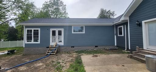 Exterior view of a blue-sided house with white trim. There are windows and a door, and some wooden steps.