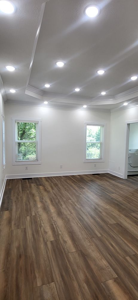 Interior of a brightly lit room with a wood floor, recessed ceiling lights, and two windows.