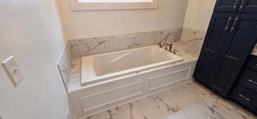 A bathroom with a white bathtub, marble countertops, and dark blue cabinets.