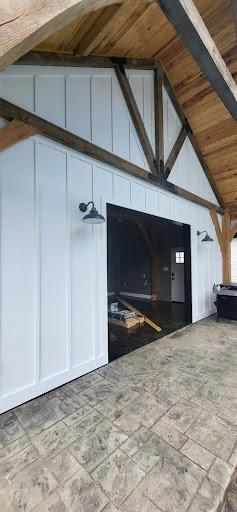 White building exterior with dark trim and lights, wooden ceiling, and stone flooring.