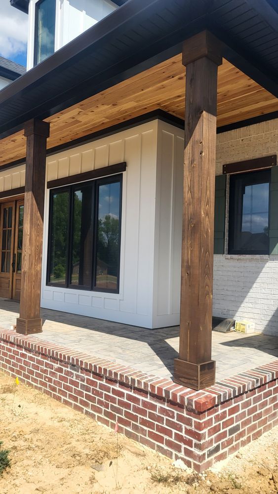 Porch of a house with brick base, white siding, dark wood columns and trim.