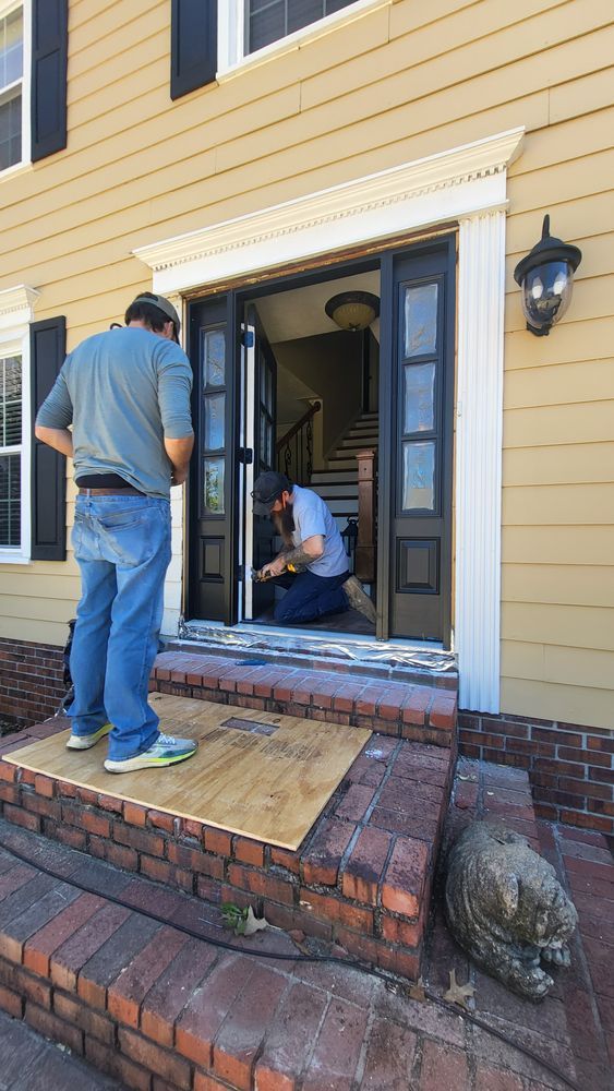 Two people working on a doorway of a yellow house. One stands on a step, the other kneels inside, near stairs.