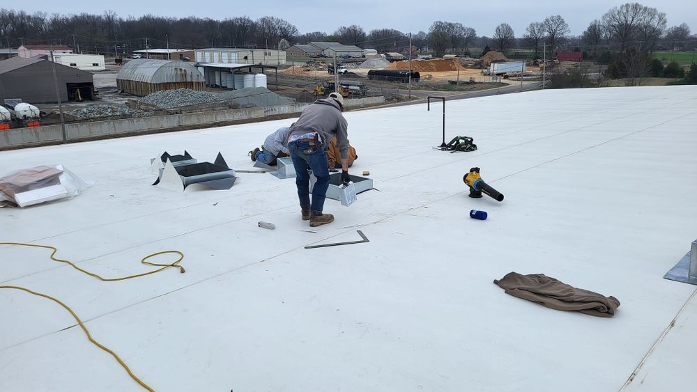 Roofer works on white flat roof with tools and materials. Buildings in the background. Overcast day.