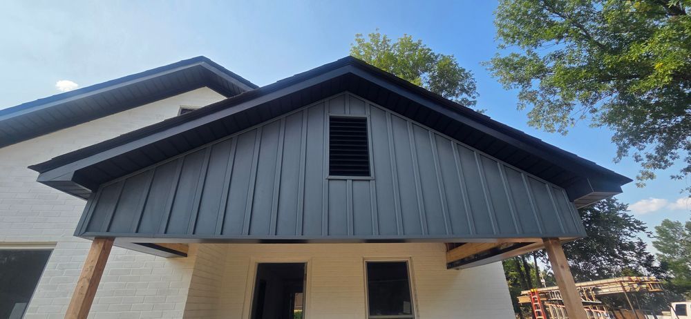 Exterior of a house with gray siding, dark trim, and a vent. Blue sky.